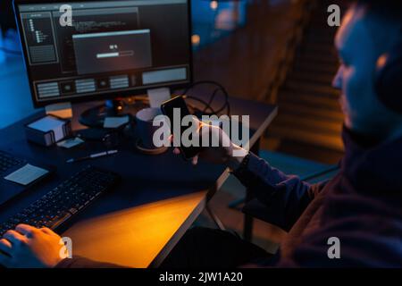 hacker with smartphone and computers in dark room Stock Photo