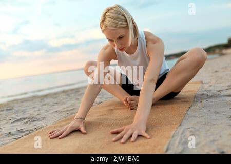 woman doing yoga stretching pose on beach Stock Photo