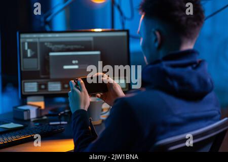 hacker with smartphone and computers in dark room Stock Photo