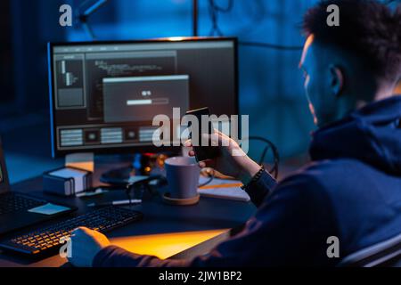 hacker with smartphone and computers in dark room Stock Photo
