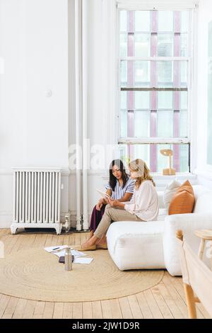 Creative businesswomen discussing over tablet PC while sitting on sofa in office Stock Photo