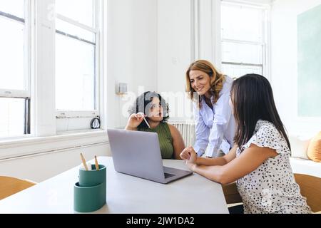 Female colleagues discussing over laptop during meeting in creative office Stock Photo