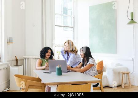 businesswoman discussing strategy with colleagues over laptop at table in creative office Stock Photo