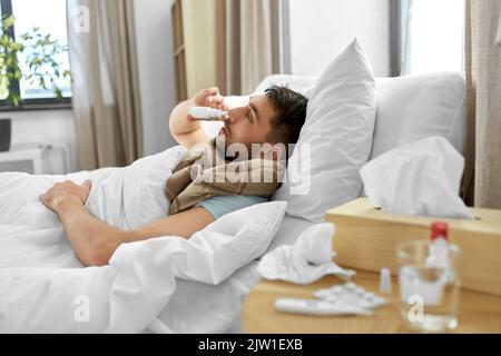 sick man with nasal spray lying in bed at home Stock Photo