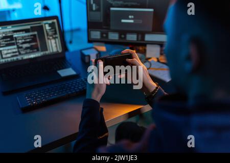 hacker with smartphone and computers in dark room Stock Photo