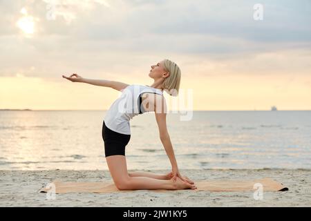 woman doing yoga camel pose on beach Stock Photo