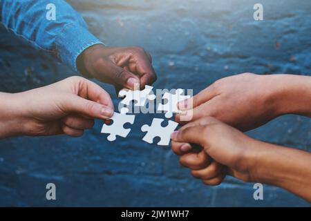Finding solutions piece by piece. four people each holding a puzzle piece to fit together. Stock Photo