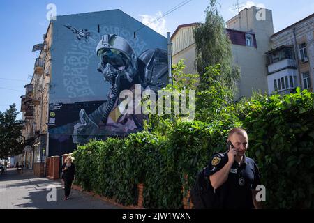 Kyiv, Ukraine. 30th Aug, 2022. A policeman walks near the mural 'Ghost of Kyiv' dedicated to Ukrainian military pilots defending the skies of Ukraine from Russian aggression. The image shows a pilot in the cockpit of the famous MiG-29 aircraft. This is a collective image of all Ukrainian military pilots of the 40th tactical aviation brigade of the Ukrainian Air Force. Credit: SOPA Images Limited/Alamy Live News Stock Photo