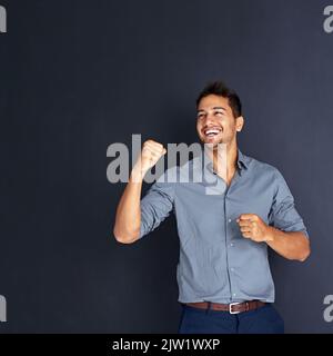 Success is yours for the taking. Studio shot of a young businessman standing with his fists raised in celebration against a dark background. Stock Photo