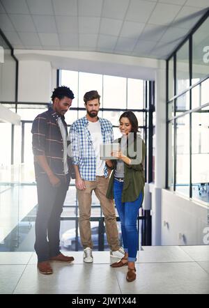 Getting creative together. three young designers working on a digital tablet in a modern office. Stock Photo