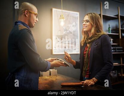 Ill take that on credit. a customer paying using NFC technology in a shop. Stock Photo