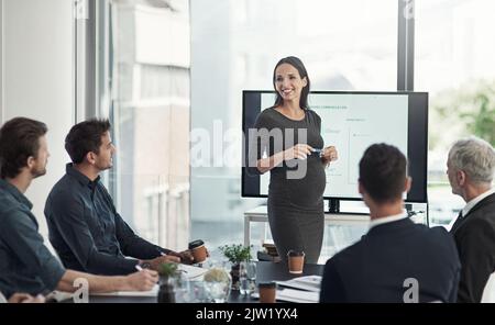 Walking them through this quarters figures. a pregnant businesswoman giving a presentation on a monitor to colleagues in an boardroom. Stock Photo