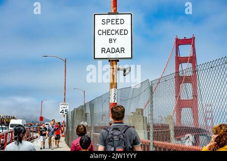 A white road sign on The Golden Gate Bridge in San Francisco warns drivers that speed will be check by radar. Stock Photo