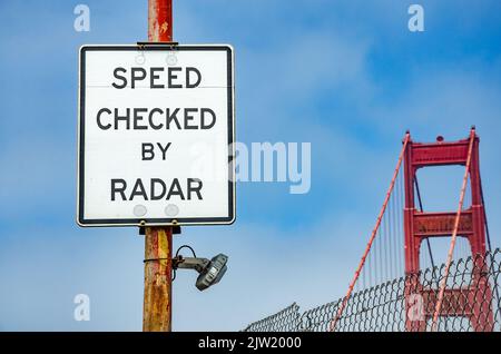 A white road sign on The Golden Gate Bridge in San Francisco warns drivers that speed will be check by radar. Stock Photo