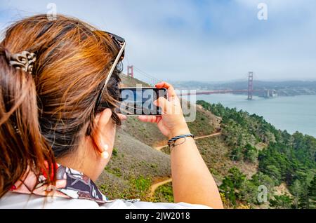 A lady takes a photo of The Golden Gate Bridge on her mobile phone while on vacation in San Francisco, California, USA Stock Photo