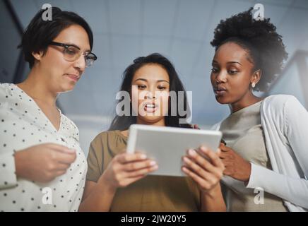 Three heads are better than one. Low angle shot of three businesswomen looking at a tablet in the office. Stock Photo