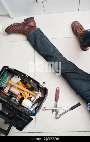 Hes got the tools to tend to your plumbing requirements. a handyman conducting repairs on the floor next to his tool box. Stock Photo