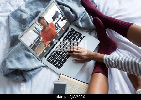 Biracial young woman video conferencing with businesswoman while working from home on bed Stock Photo