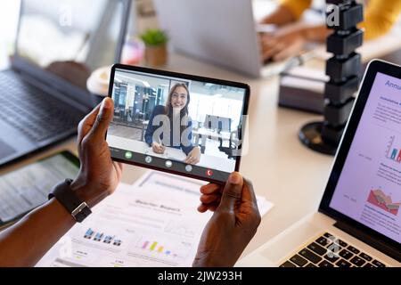Cropped hands of african american man holding digital tablet while video calling female colleague Stock Photo