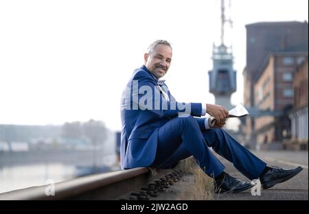 Man in blue suit sitting on railway track reading newspaper, Rheinhafen, Karlsruhe Stock Photo