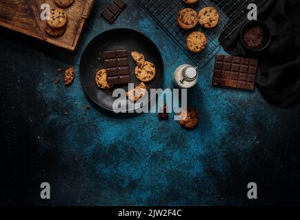 Top view of glass of fresh milk placed on dark blue table near yummy biscuits and chocolate bars Stock Photo