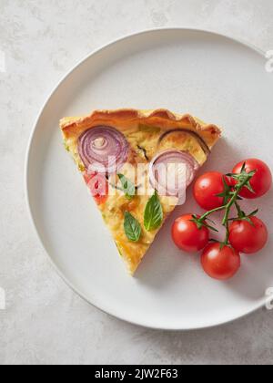 Top view of piece of delicious quiche and bunch of cherry tomatoes served for lunch on plate Stock Photo