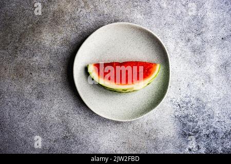 From above still life composition of sliced ripe striped green watermelon placed on stone plate on concrete background Stock Photo
