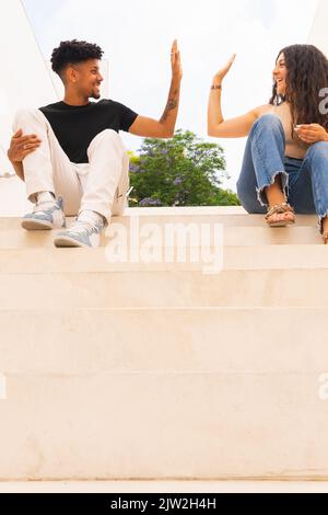 Smiling young couple doing high-five while sitting on steps Stock Photo