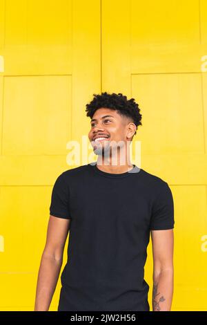 Happy young man looking away while standing against yellow wall Stock Photo