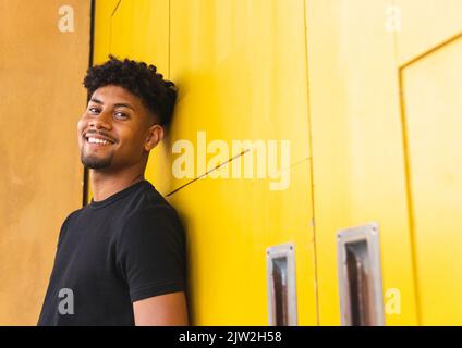 Happy young man looking at camera while standing against yellow wall Stock Photo