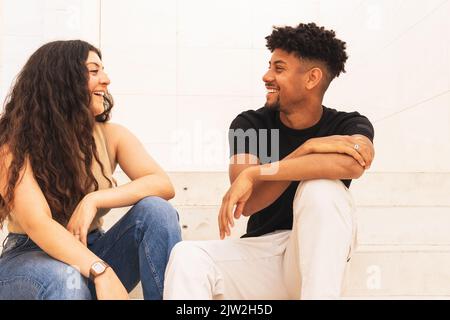Smiling young couple talking while sitting on steps Stock Photo