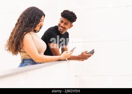 Smiling young man looking at girlfriend using smartphone while standing in balcony Stock Photo