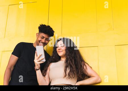 Smiling young woman showing smartphone to boyfriend while standing by wall Stock Photo