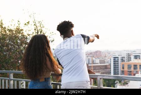 Rear view of young man pointing at city while standing with girlfriend in city Stock Photo