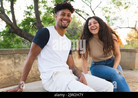 Portrait of cheerful young couple laughing while sitting at park Stock Photo