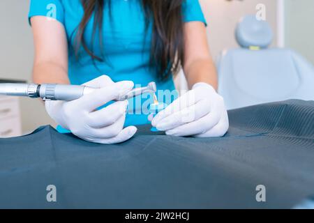 Cropped unrecognizable female dentist with long dark hair in blue uniform and latex gloves smiling while working in modern clinic and using dental dri Stock Photo