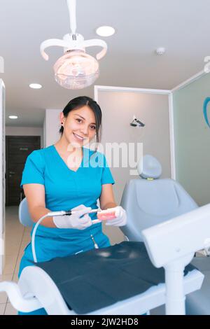 Young ethnic hispanic female dentist using dental drill while practicing treatment on denture during work in modern clinic Stock Photo