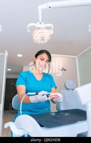 Young ethnic hispanic female dentist using dental drill while practicing treatment on denture during work in modern clinic Stock Photo