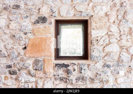 Rectangular window with black frame installed on rough stone wall of old building Stock Photo
