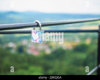 Locked lock hangs on the metal fence. Symbol of love in the park. The metal red lock in the shape of a heart is locked with a key Stock Photo