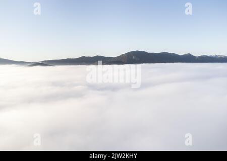 Breathtaking view of white clouds floating against mountain peaks and blue sky in daytime in highlands Stock Photo