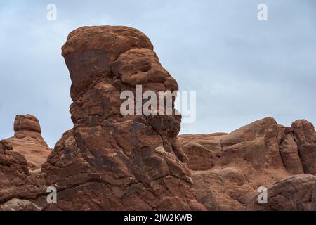 Uneven Balanced Rock formation resembling human face against cloudy gray sky in Arches National Park in Utah, USA Stock Photo