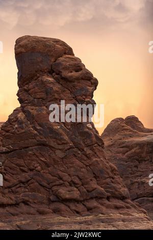 Uneven Balanced Rock formation resembling human face against cloudy gray sky in Arches National Park in Utah, USA Stock Photo