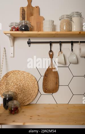 Various kitchen supplies and glass jars with assorted ingredients placed on wooden shelves against white wall Stock Photo