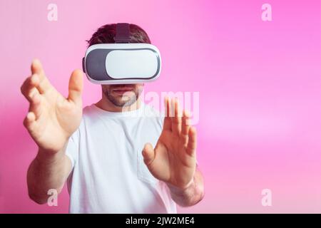 Serious male gamer in modern VR headset exploring cyberspace on pink background in light studio Stock Photo