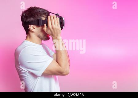 Serious male gamer in modern VR headset exploring cyberspace on pink background in light studio Stock Photo