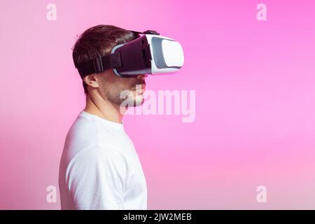 Serious male gamer in modern VR headset exploring cyberspace on pink background in light studio Stock Photo