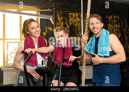 Cheerful young sportsman and sportswomen with towels smiling and looking at camera while exercising during training in gym Stock Photo