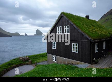 Picturesque view of stone house with mossy roof located against waving sea and cloudy sky behind window of old building on stormy day on Faroe Islands Stock Photo
