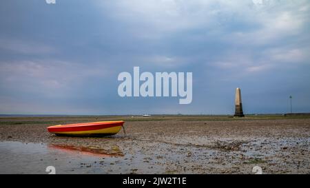 A rowing boat lies stranded at low tide next to The Crow Stone, the old marker for the limit of the Port of London in the Thames Estuary at Chalkwell Stock Photo